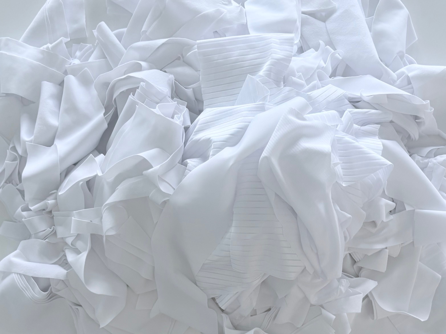 Primer plano de recortes de poliéster blanco puro en el taller de fabricación textil de Negua en España. Se aprecian las diferentes texturas de los restos de tejido pre-confección organizados para su reciclaje en origen.